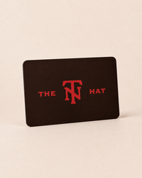 A black rectangular card or coaster with rounded corners, standing upright on a light beige background. The card features the red text 'THE TN HAT' with a stylized 'TN' logo in the center.