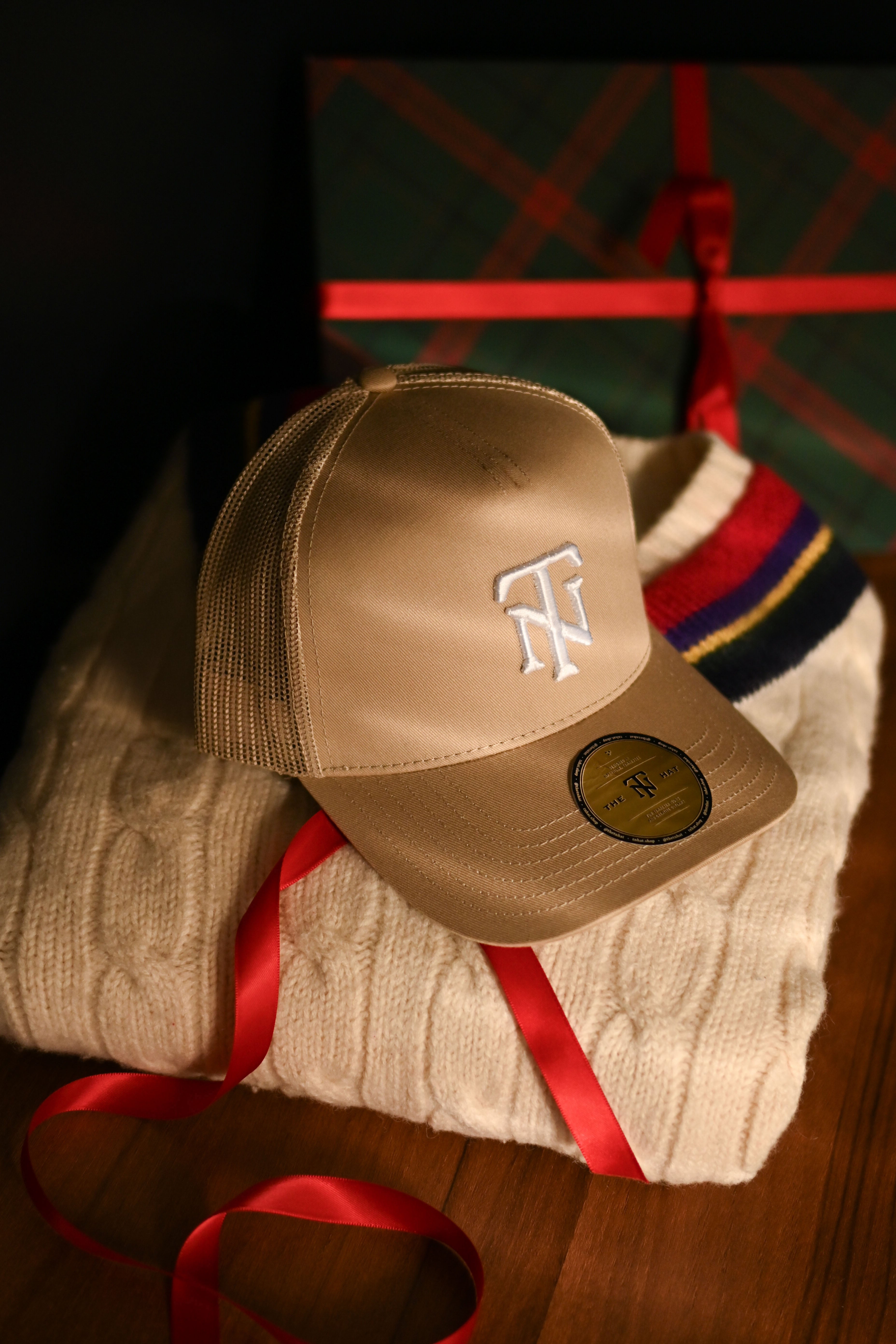 Beige cap with logo on a white surface with red ribbons